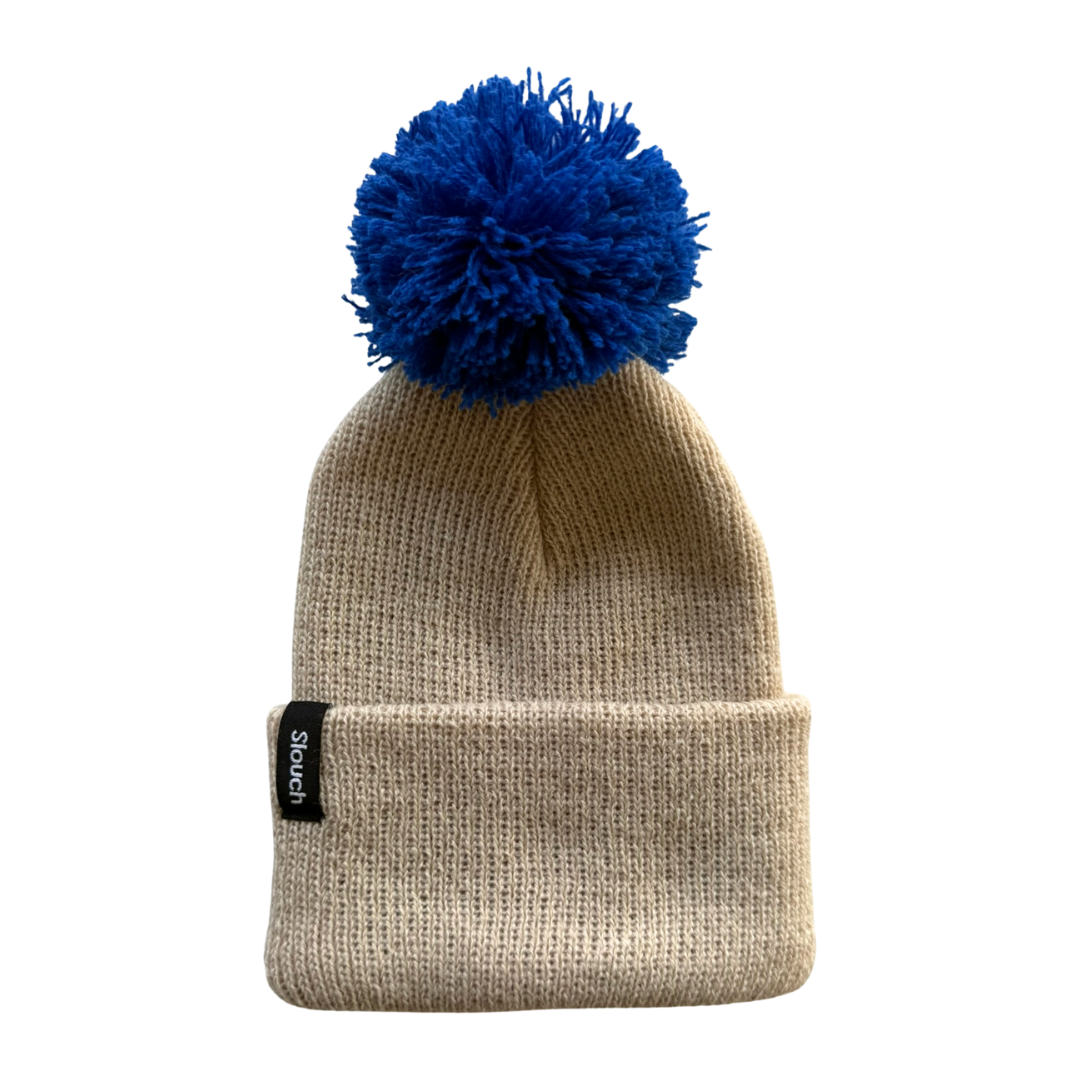 Beige knit beanie with a blue pom-pom on a white background